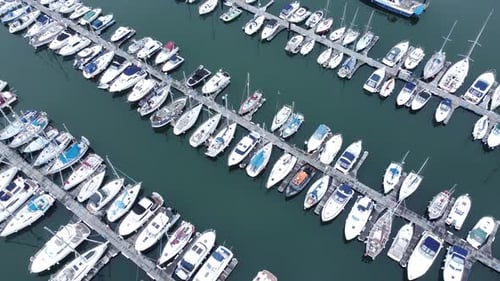 Top down aerial view above luxury yachts parked on turquoise ocean water marina rotating right shot