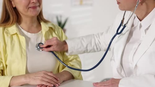Cardiologist with stethoscope listening patient's heartbeat at table in clinic, closeup