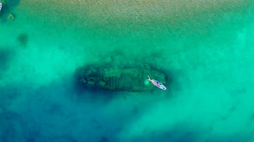 Paddleboarder Over Sunken Ship in Turquoise Sea