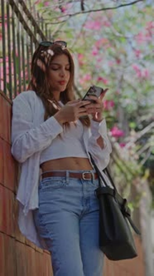 Young Woman Typing a Message on Her Phone While Standing on a City Street