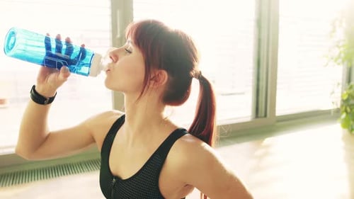 Woman Drinking Water after Exercise in Bright Studio