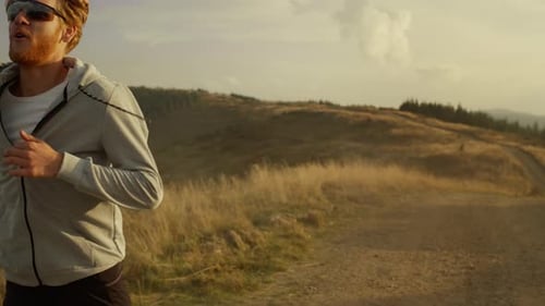 Redhead sportsman enjoying cardio workout running on mountain road in summer morning