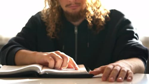 Ein bärtiger Mann mit lockigem Haar liest die christliche Bibel und liest das Wort Gottes