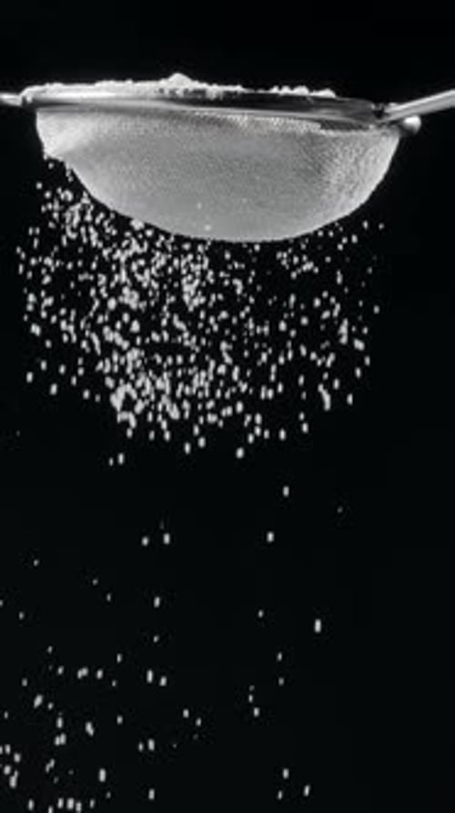 Sifting White Powder Through Sieve on Black Background