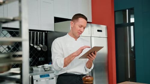 Professional chef using tablet computer for recipes while working in modern kitchen cooking concept