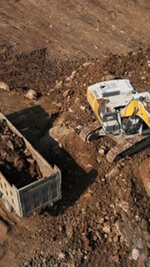 Excavator Filling Truck with Dirt on Construction Site
