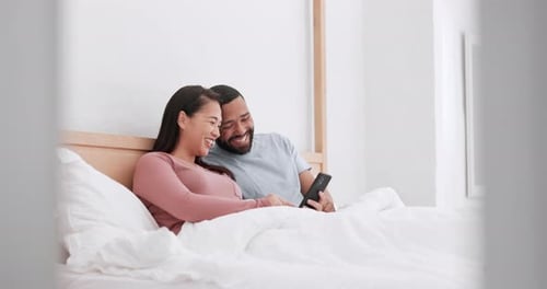 Laughing Couple Relaxing Together in Bed with Phone