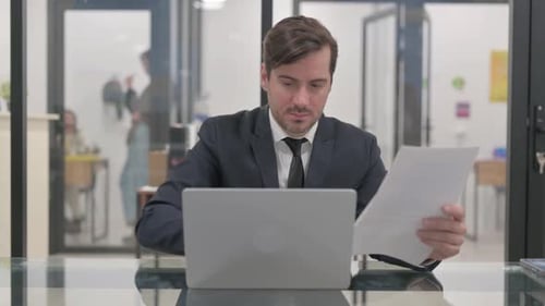 Man Working At Desk with Laptop and Papers