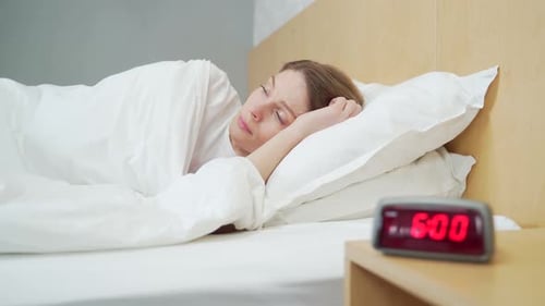 Close up portrait of sleeping woman in bed at home wakes up from the loud sound of the alarm clock