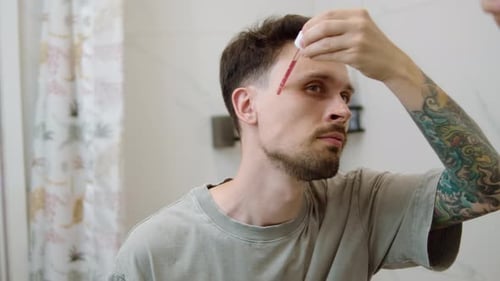 Man Applying Red Liquid to Forehead in Bathroom