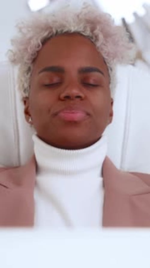 Une femme aux cheveux bouclés se détend les yeux fermés dans une pièce lumineuse