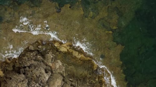 Aerial descending view looking down over Mallorca ocean waves crashing against rocky coastal shoreli