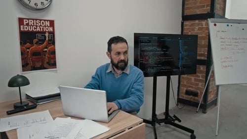 Male Programming Teacher Sitting at Desk in Prison Classroom during Lesson
