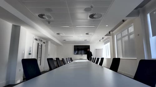 Businessman walking around long corporate meeting table in empty office