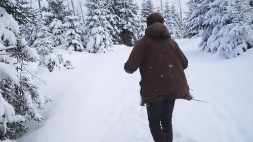 Caucasian man in casual winter clothing walking in winter forest path and putting on brown winter ja