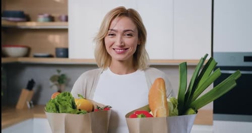 Woman Smiling Holding Bags of Groceries in Kitchen