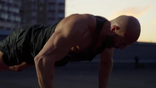 Muscular Man Doing Pushups on Rooftop at Sunset