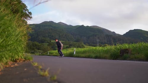 Man rides his skateboard in the road with mountains in the background