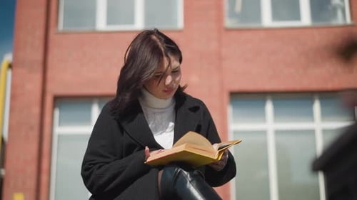 Young Woman Reads Book Outside Brick Building