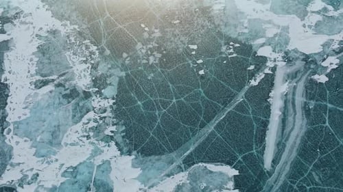 Aerial view of cracked turquoise ice with snow patches on Lake Baikal surface