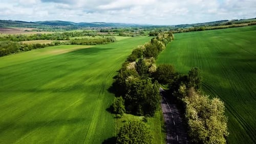 Aerial landscape shot of cloudy bright and shady view of agricultural areas hills following road sum