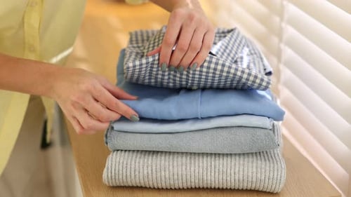 Woman with stack of clothes near window indoors, closeup