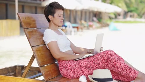 4K Asiatin arbeitet in den Sommerferien am Strand am Laptop.