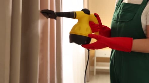 Woman Steaming Curtains with Steam Cleaner Indoors