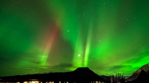 Mesmerizing aurora borealis flaring in starlit sky, time lapse over Balsfjord