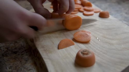 Slicing fresh carrot on wooden board with knife