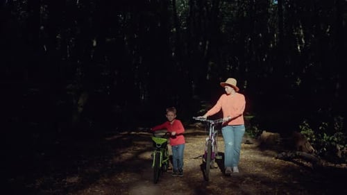 Mother and Son Go for a Walk with Bicycles in the Summer Forest
