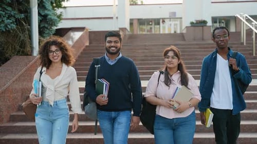 Four Multi Ethnic University Students with Books and Backpacks Smiling While Walking Down the Stairs
