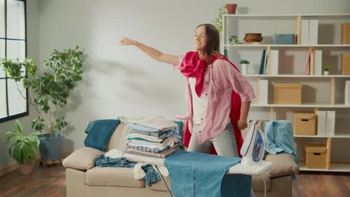 Happy Woman in Super Hero Cape Dancing While Ironing Clothes at Home