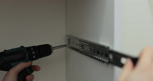 Homme utilisant une perceuse électrique pour fixer une glissière de tiroir en métal à un meuble pendant l'assemblage