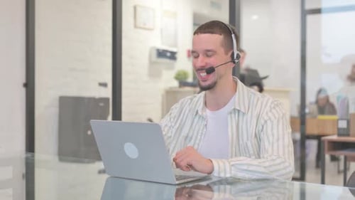 Creative Young Man with Headset Doing Video Chat on Laptop in Call Center