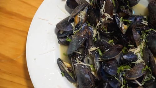 Plate of freshly steamed mussels in white wine sauce with herbs and cheese, close up slider HD