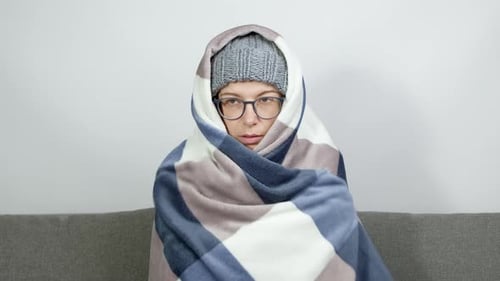 A woman wrapped in a blanket warms herself while sitting in a cold room in winter.
