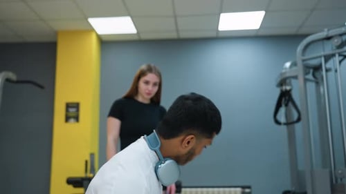 Man Doing Squat Exercise While Woman Watches Attentively During Gym Training Session