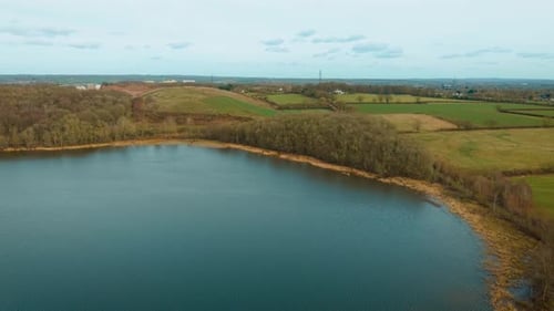 Vue aérienne du lac avec rivage incurvé bordé de forêts et de roseaux secs, terres agricoles vertes et dorées