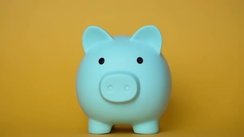 Hand inserting coin into light blue piggy bank on yellow background