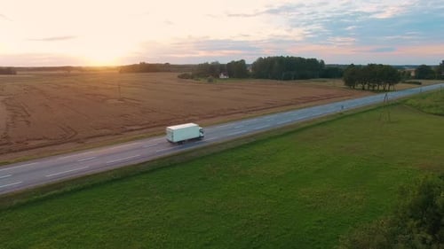 Following and Aerial Shot of a Truck Driving on Highway. Beautiful Field Landscape and Setting Sun.