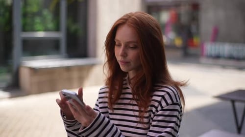 Pensive Pretty Woman with Redhaired Sitting at Table of Outdoor Cafe and Writing Text Message on