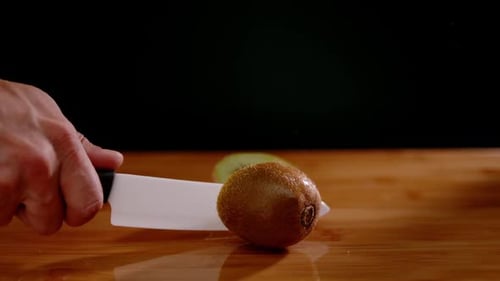 Sharp chef knife slice kiwi in half with power, super slow motion view