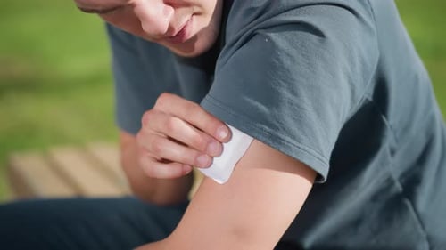 Young Adult Applying Bandage to Arm Outdoors