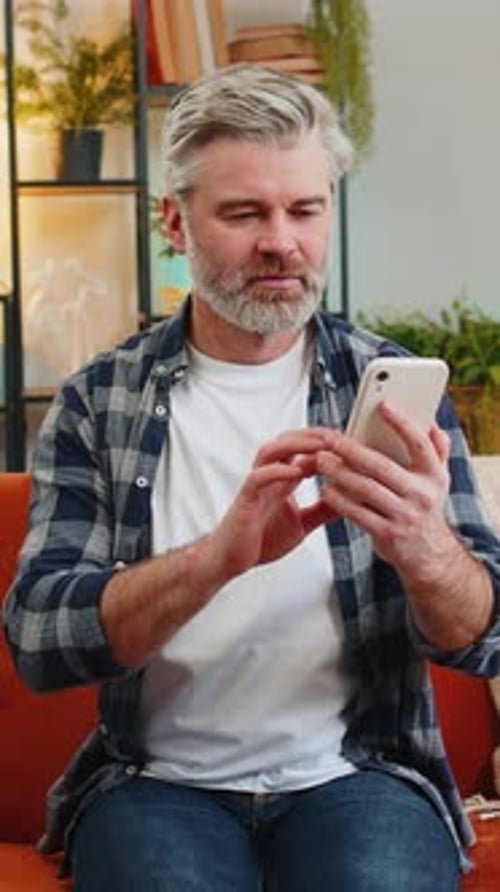 Man Relaxing Indoors and Typing on Mobile Phone