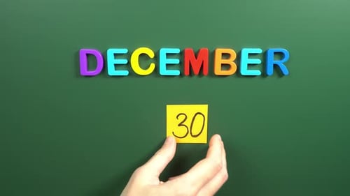 Hand sticking a sticker 30 December calendar day on school board. 30 date of December. Thirtieth