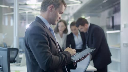 Businessman Working on Tablet in Crowded Office
