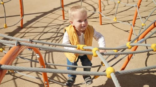 Cute baby boy playing on the playground and climbing up the rope spider web