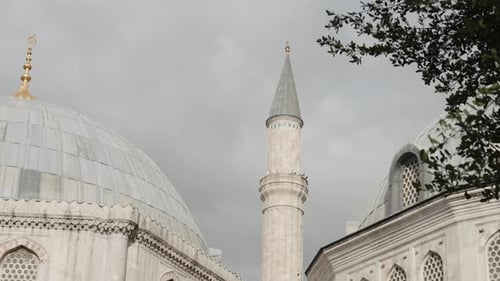 Minaret of a mosque on a cloudy sky background. Action. Summer green trees and mosque building.