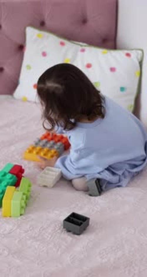 Una niña pequeña juega a construir en la cama con ladrillos de juguete